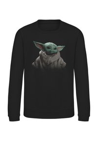 Svart sweatshirt med en grafik av en liten, gröngömd karaktär med stora ögon och framträdande öron, iklädd en ljusfärgad mantel.