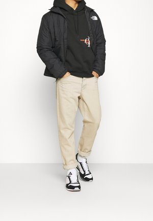 Schwarze Steppjacke, schwarzer Hoodie mit Grafik, hellbeige, weit geschnittene Jeans und schwarze Sportschuhe mit weißen Akzenten. Minimalistisches Design.