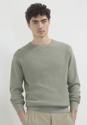Light green knit sweater with ribbed texture, round neckline, and long sleeves. Features elastic cuffs and waist, styled simply with no patterns.