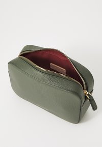 Pochette cosmetica verde in pelle con finitura testurizzata, dettagli con zip dorata e interno in tessuto bordeaux. Include un tirazip.
