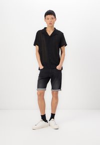 Black short-sleeve button-up shirt with a textured pattern, paired with dark denim shorts that are rolled at the hem and white sneakers.