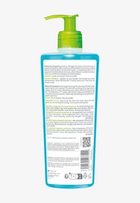 Bottiglia trasparente con base turchese e pompa verde. Presenta testo multilingue e un codice QR sul retro.