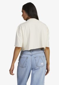 Cropped cream t-shirt made of cotton with short sleeves, paired with light blue high-waisted jeans featuring back pockets and a distressed detail.