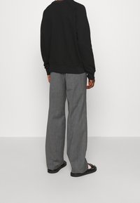 Felpa nera con orlo a coste, abbinata a pantaloni ampi grigi chiari. L'outfit presenta sandali neri flat e un design minimalista.