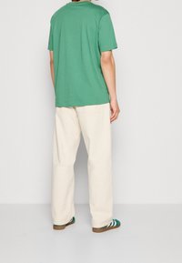 Grön kortärmad t-shirt kombinerad med ljusbeiga vida byxor. Outfiten kompletteras med skor med gröna och vita ränder.