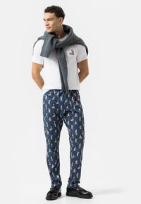 Witte t-shirt met grafisch ontwerp, grijze gebreide sjaal, marineblauwe broek met patroon en kleurrijke print, en zwarte schoenen.