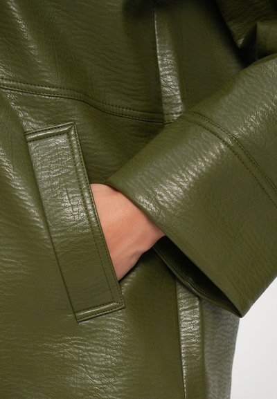 Giacca in pelle verde oliva con finitura testurizzata, dotata di tasca laterale e polsini larghi. La superficie presenta una leggera lucentezza e cuciture visibili.