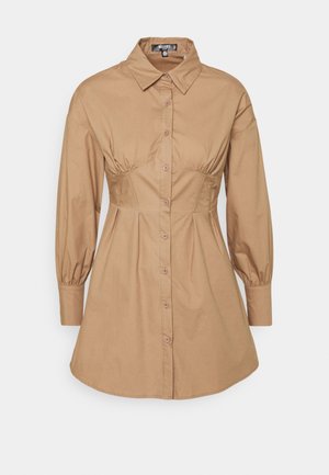 Długa, zapinana na guziki, tanowa sukienka koszulowa z długim rękawem, zaostrzonym kołnierzykiem i dopasowanymi szwami w talii, lekko rozkloszowanym dołem oraz mankietami.