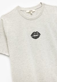 Grijs T-shirt met korte mouwen van zachte stof, met een zwart lippen graphic op de borst. Eenvoudige ronde halslijn en een relaxte pasvorm.