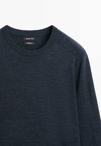 Blå ulltröja med rund halsringning, med en mjuk textur och raglanärmdesign. Etiketten lyder "Massimo Dutti, 100 % merinoull."