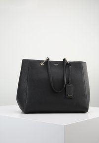 Svart syntetisk toteväska med dubbla handtag, guldfärgad hårdvara, texturerad yta och en dekoration med DKNY-logotypen.