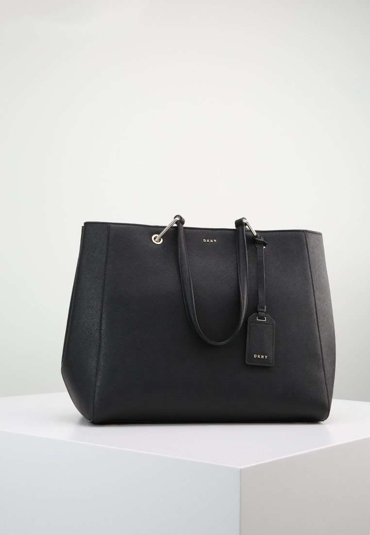 Svart syntetisk toteväska med dubbla handtag, guldfärgad hårdvara, texturerad yta och en dekoration med DKNY-logotypen.