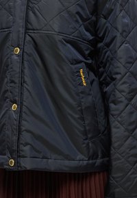 Tengerészkék steppelt dzseki aranyszínű kapcsokkal, bal oldalon zsebbel, melyen sárga "Barbour" logó található. Sima, vízálló anyagból készült.