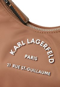 Rudas nailono rankinė su sidabriniu įspaustu tekstu: "KARL LAGERFELD PARIS 21 RUE ST-GUILLAUME." Su užtrauktuku ir odiniais akcentais.