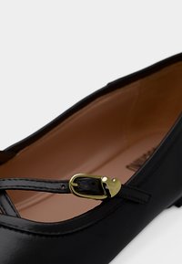 Μαύρο δερμάτινο παντόφλα με λεπτό λουράκι που φέρει μικρή χρυσή αγκράφα σε σχήμα καρδιάς.