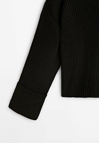 Black ribbed knit sweater sleeve with a wide, textured cuff and a relaxed shape. Material appears soft with a thick, cozy texture.