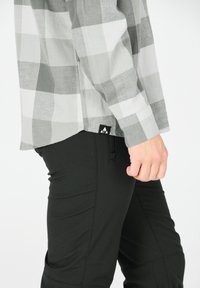 Grå plaid skjorte med lange ærmer, parret med sorte tætsiddende bukser med en lynlåslomme og et logo mærke nær kanten.