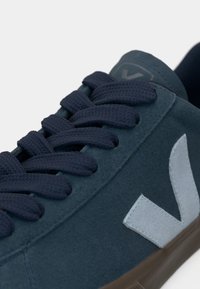 Tenisi din suede bleu închis cu șireturi din textil și un accent de logo bleu deschis. Au vârf rotund și o talpă din cauciuc maro cu textură minimă.