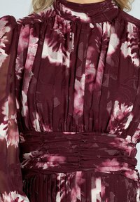 Vestido de estampado floral en color burdeos con textura plisada, cuello alto y cintura fruncida. Mangas largas transparentes con detalles florales.