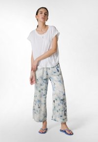 Biała, luźna koszulka; jasno-niebieskie, kwiatowe spodnie typu wide-leg; fioletowe klapki; miękkie, wygodne materiały.