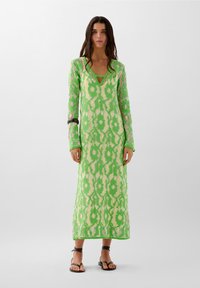 Gebreide groene jurk met lange mouwen, V-hals en bloemmotief. Heeft een losse pasvorm, ingewikkelde textuur en een lengte tot de knie.