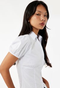 Witte button-up shirt met pof korte mouwen, gestructureerde pasvorm en een gladde textuur. Ontworpen met een klassieke kraag en subtiele naden.