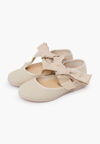 Ballerine in tessuto beige con tomaia testurizzata, punta tonda e fetti a fiocco prominenti sulle cinghie. Foderatura interna morbida.