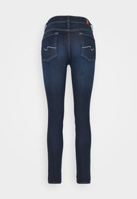 Jeans de mezclilla ajustados en azul oscuro con una textura suave. Presenta costuras decorativas en los bolsillos traseros y una cintura de altura media.