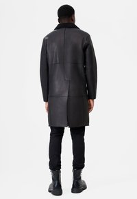 Black leather coat with a textured surface, featuring a contrasting collar, long sleeves, and geometric patchwork design.