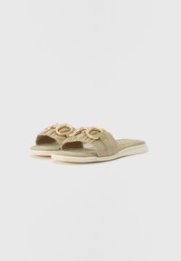 Sandale slip-on din suede verde, cu o bandă texturată și accente circulare aurii pe partea superioară. Tălpică căptușită și talpă de culoare deschisă.