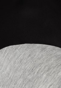 Tela negra y gris mostrando una textura suave; el gris es jaspeado y curvado en el borde, contrastando con la sección negra sólida.