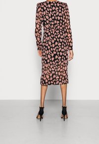 Maxi šaty z průhledné černé látky s růžovým puntíkovaným vzorem, s dlouhými rukávy, staženým pasem a délkou po lýtka. V kombinaci s černými vysokými podpatky.