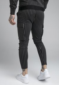 Svartrandiga joggers med slim fit och cargofickor, med en texturerad midja och tillsammans med vita sneakers.
