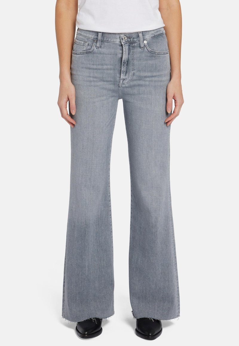 Jeans évasés gris clair en denim avec une texture délavée, comportant cinq poches, une fermeture à zip et des détails d'ourlet brut.