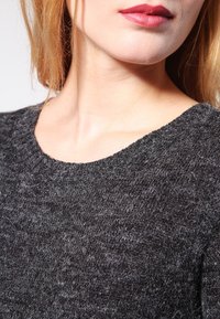 Maglione lavorato a maglia grigio scuro con scollatura rotonda e finitura testurizzata, realizzato in un tessuto morbido e peloso con fibre visibili.