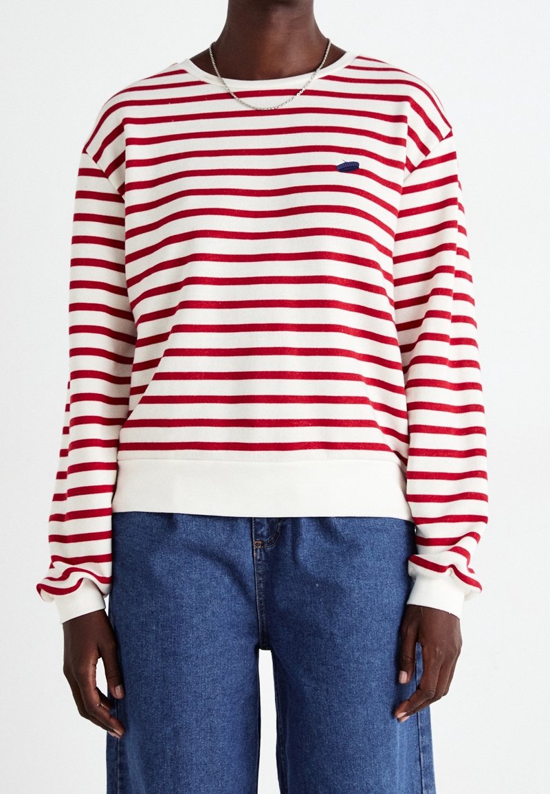 Sweat-shirt rayé rouge et blanc avec un col rond côtelé, des manches longues et un petit logo bleu sur la poitrine. Associé à un jean en denim bleu.