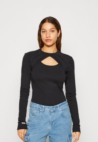 Maglietta nera a maniche lunghe con scollatura rotonda e un dettaglio di apertura frontale. Tessuto morbido, design aderente e pantaloni cargo in denim blu a contrasto.