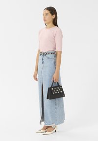 Light pink fitted top and high-slit denim skirt paired with a studded black handbag and cream pointed-toe heels.