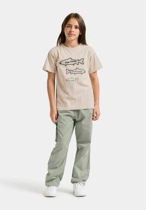 Beige katoenen T-shirt met vissersthema in zwarte opdruk. Lichtgroene nylon broek, losse pasvorm, met zijzakken en zwarte accenten. Witte sneakers.