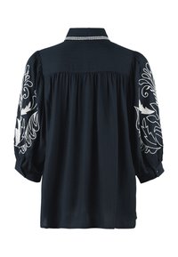 Blouse noire avec broderie florale blanche sur manches ballon, coupe ample, empiècement aux épaules et surpiqûres blanches au col.