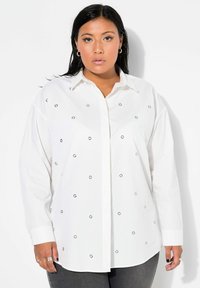 Camisa blanca de botones con embellishments circulares plateados por toda la prenda. Presenta un cuello clásico y mangas largas, hecha de una tela ligera.