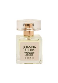 Przezroczysta butelka perfum o kwadratowym kształcie, złoty akcent na głowicy sprayu oraz biała etykieta z napisem "JOANNA KRUPA FEMININE POWER ESOTIQ."
