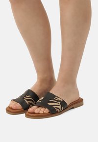 Sandales à glissière noires et beiges avec un dessus en textile à motif zèbre, bout ouvert, semelle plate et un design à large bandage.