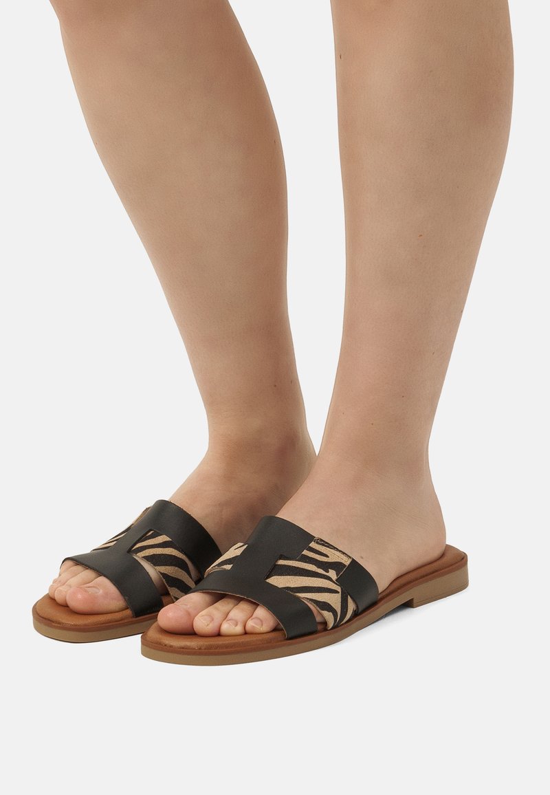 Sandales à glissière noires et beiges avec un dessus en textile à motif zèbre, bout ouvert, semelle plate et un design à large bandage.