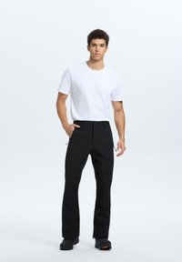 Czarne spodnie sportowe z zamkami przy kieszeniach, zestawione z gładką, białą koszulką z okrągłym dekoltem. Spodnie mają prosty krój.