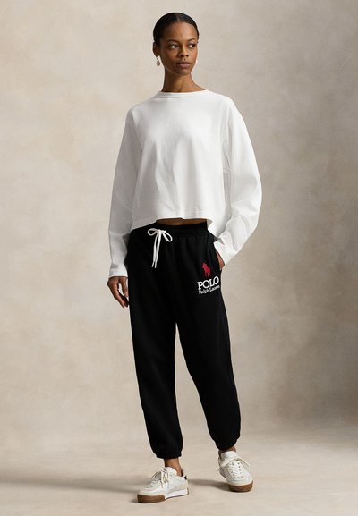 Balts īsais džemperis ar garām piedurknēm; melnas sporta bikses ar baltu un rozā "Polo Ralph Lauren" logotipu; balti sporta apavi ar brūnām zolēm.