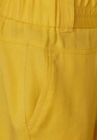 Gele katoenen blend broek met een elastische tailleband, zijzakken en een gladde textuur met gestikte details.