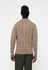 Beige Strickpullover mit gerippten Bündchen und Saum. Weicher, strukturiert Stoff. Rückansicht zeigt ein aufwendiges Muster und einen runden Halsausschnitt.