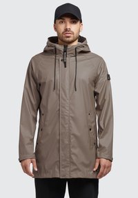 Vandtæt beige jakke med hætte, frontlynlås og to sidelommer. Har sorte snore og detail på ærmet.