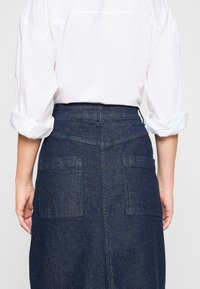 Denimkjol i mörkblå färg, hög midja, bakfickor och rak passform. Matchad med en vit skjorta med uppvikta ärmar.